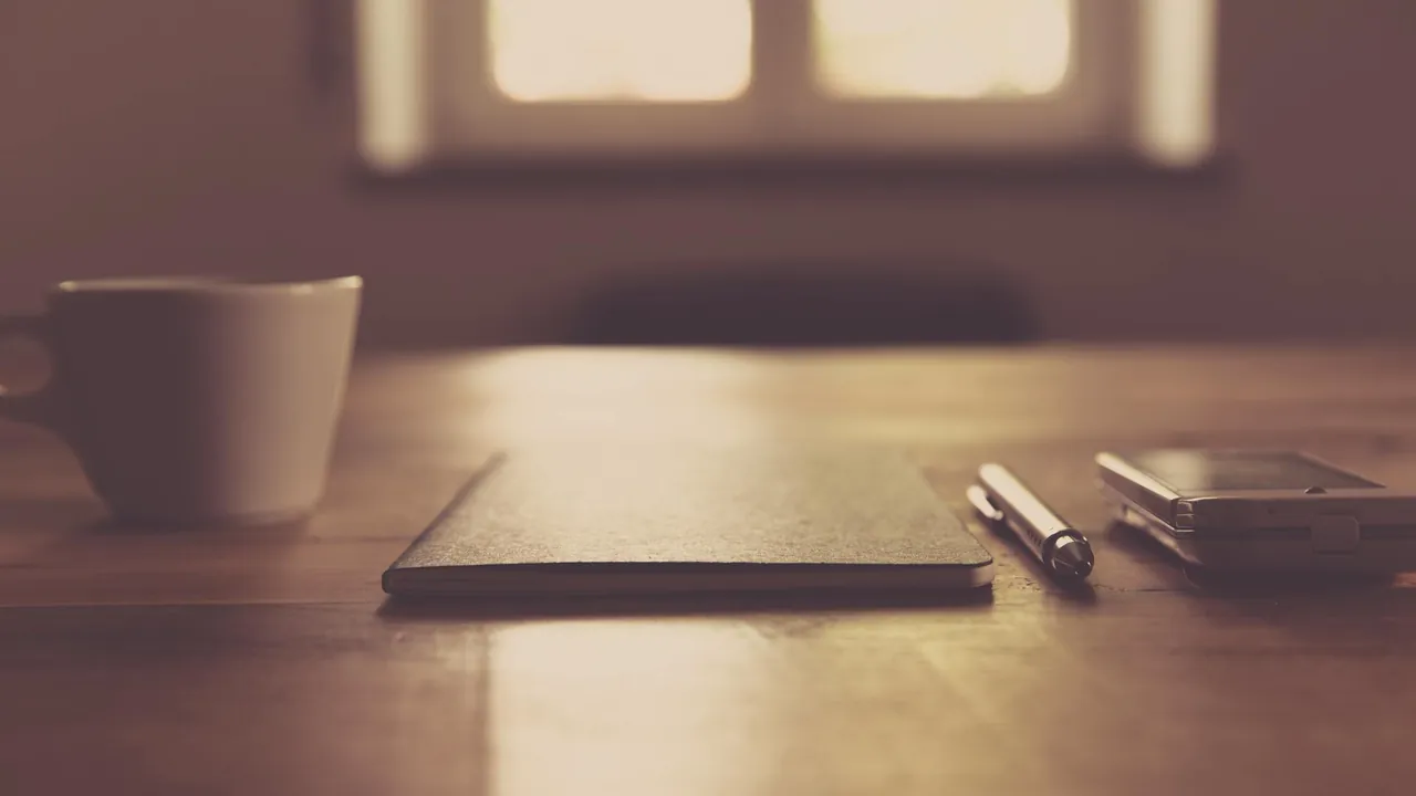 Notizbuch, Stift und Tasse auf einem Holztisch am Fenster